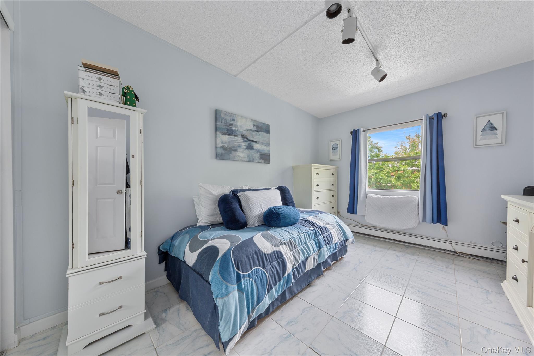 71-28 Sutton Place, Unit 3 Queens, NY 11365 - Photo 14 of 23 Bedroom with light marble finish floors, baseboard heating, rail lighting, a textured ceiling, and baseboards