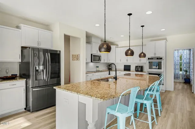 a kitchen with stainless steel appliances granite countertop a stove top oven a sink a dining table and chairs with wooden floor