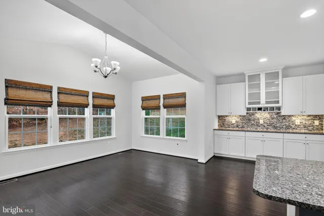 a view of an empty room with wooden floor and a kitchen