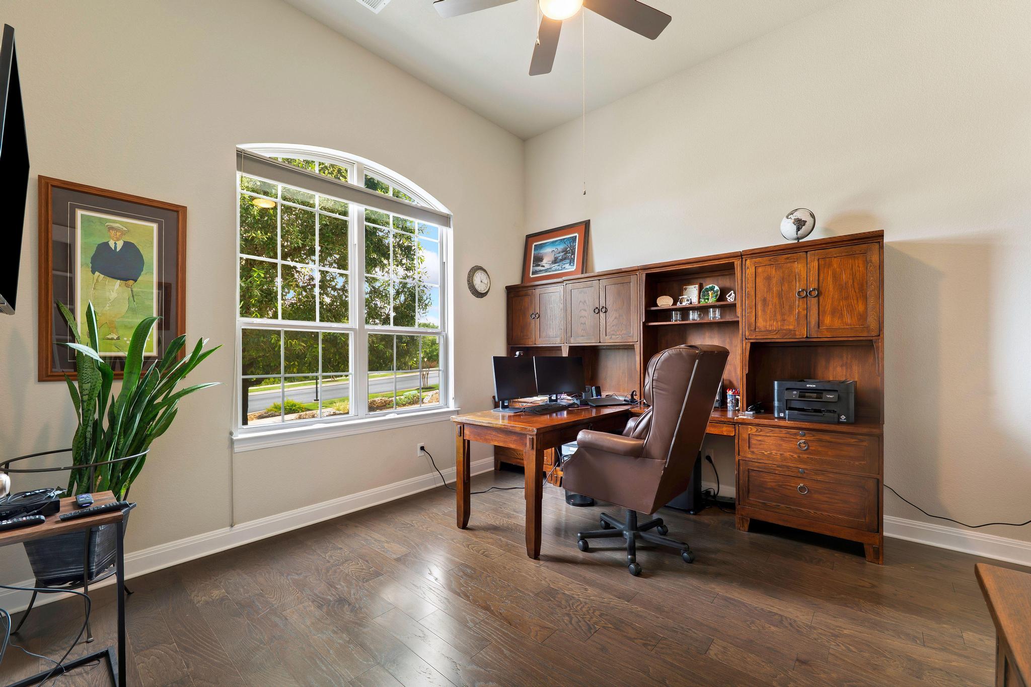 1009 Legacy Crossing Georgetown, TX 78628 - Photo 5 of 40 A dedicated home office featuring rich hardwood flooring and a large arched window that fills the space with natural light.