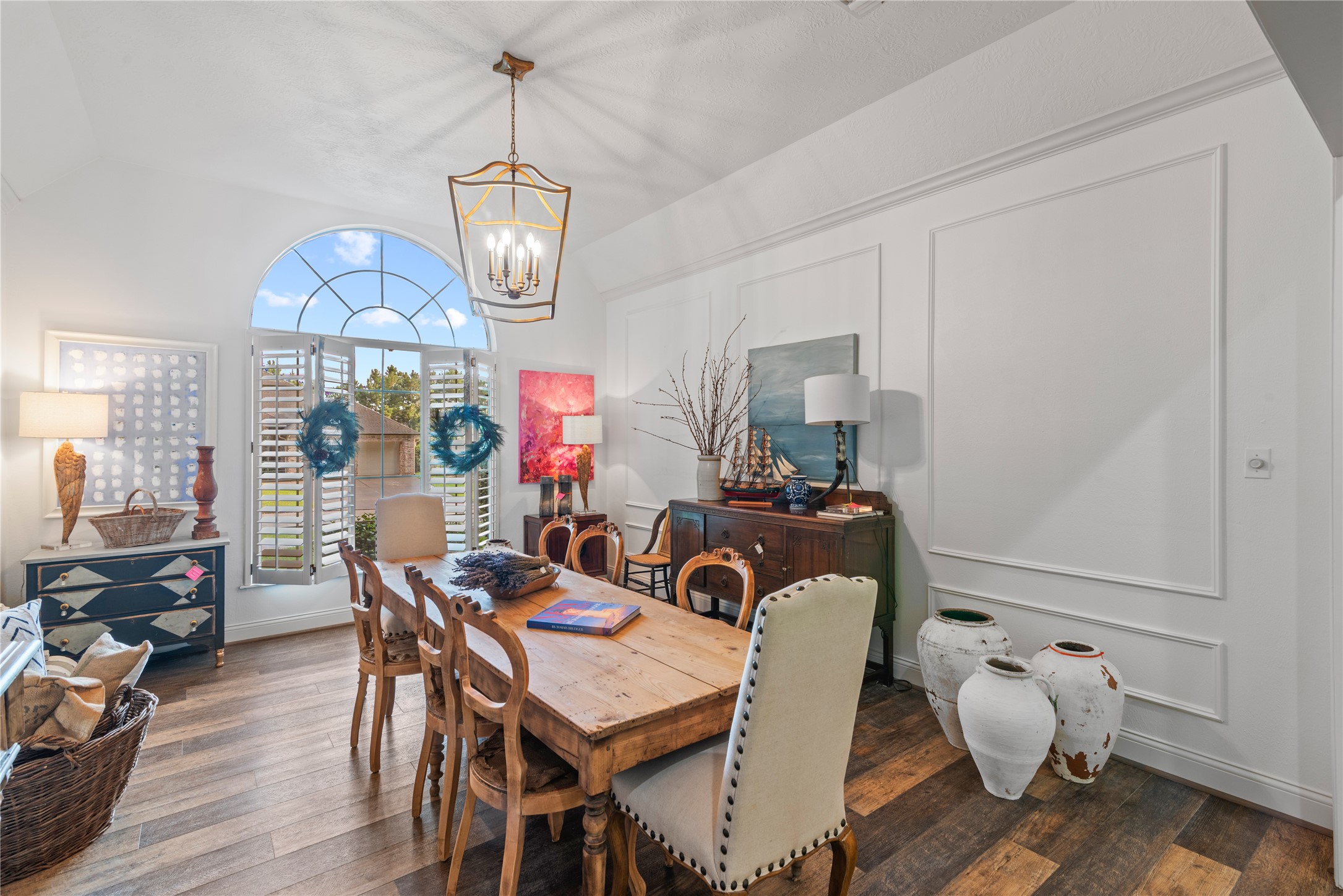 901 Longmire Road, Unit 51 Conroe, TX 77304 - Photo 27 of 48 Large arched window with plantation shutters, elegant wainscoting, and a rustic wooden table, complemented by stylish decor and a warm, inviting atmosphere in your formal dining area that opens to the living area and fireplace.
