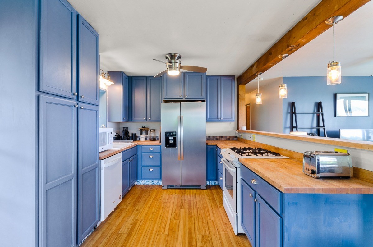 83-5434-C Middle Keei Road Captain Cook, HI 96704 - Photo 9 of 30 a kitchen with stainless steel appliances granite countertop a refrigerator a sink dishwasher a stove and white countertops with wooden floor