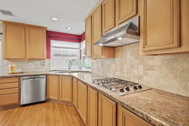 a kitchen with stainless steel appliances granite countertop a sink a stove and a wooden floors