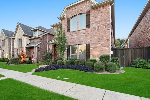 a view of a brick house with a yard plants and a large tree