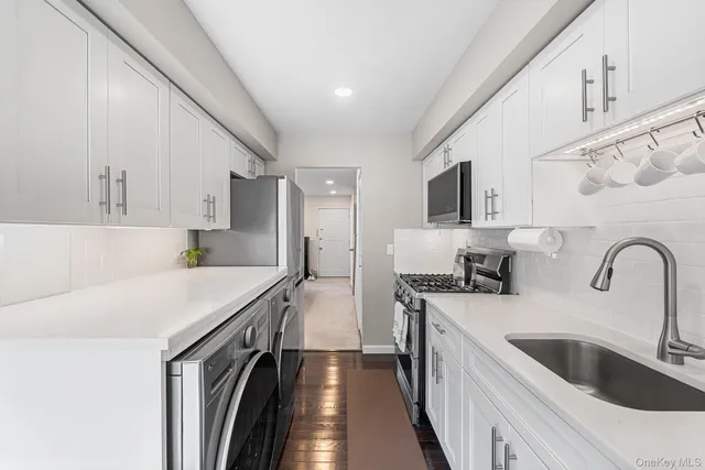 a kitchen with stainless steel appliances granite countertop a sink stove a refrigerator a oven with white cabinets and wooden floor