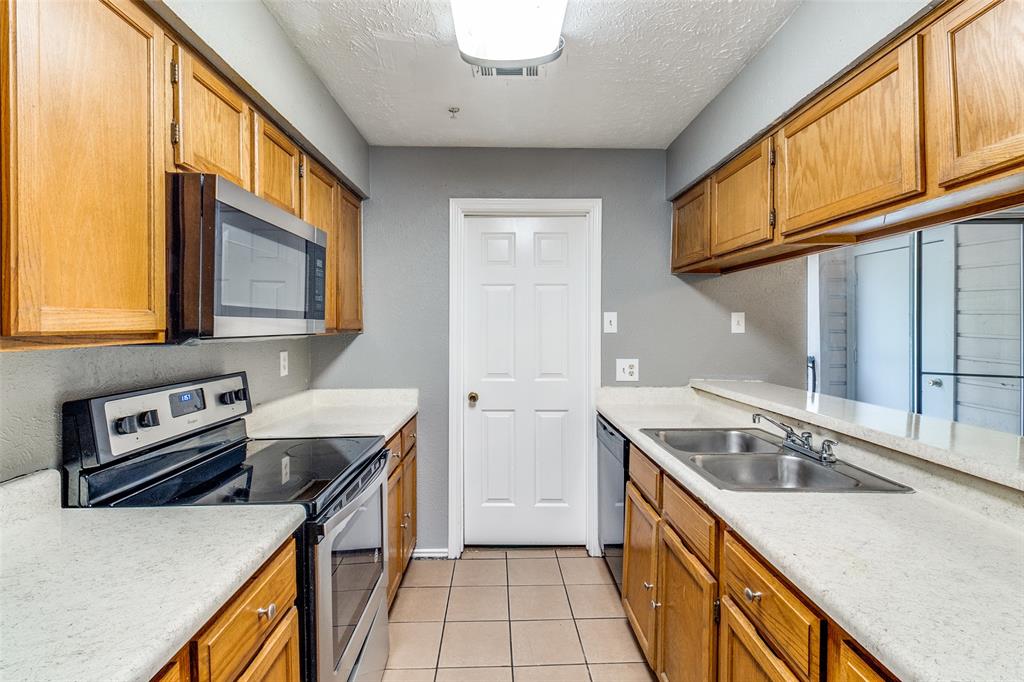 2354 Little Pocket Road, Unit B Dallas, TX 75228 - Photo 7 of 12 Kitchen featuring stainless steel appliances, a textured ceiling, light tile patterned floors, and wood finish cabinets
