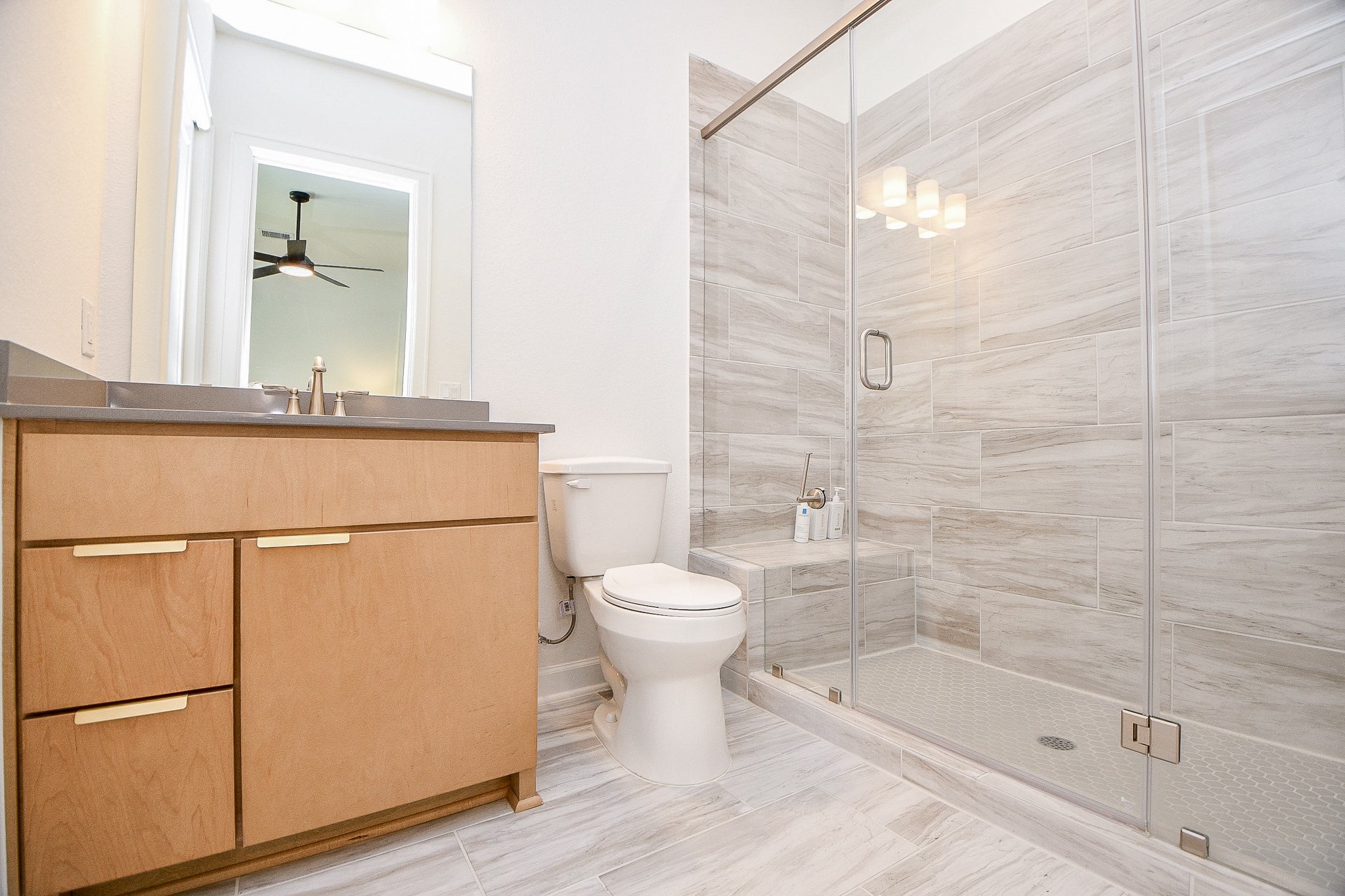 5315 Jason Street Houston, TX 77096 - Photo 17 of 39 This modern bathroom features a sleek glass-enclosed shower with elegant marble-style tiling. It includes a wooden vanity with a dark countertop, under-sink storage, and a large mirror. The space is bright and contemporary, perfect for a stylish home.