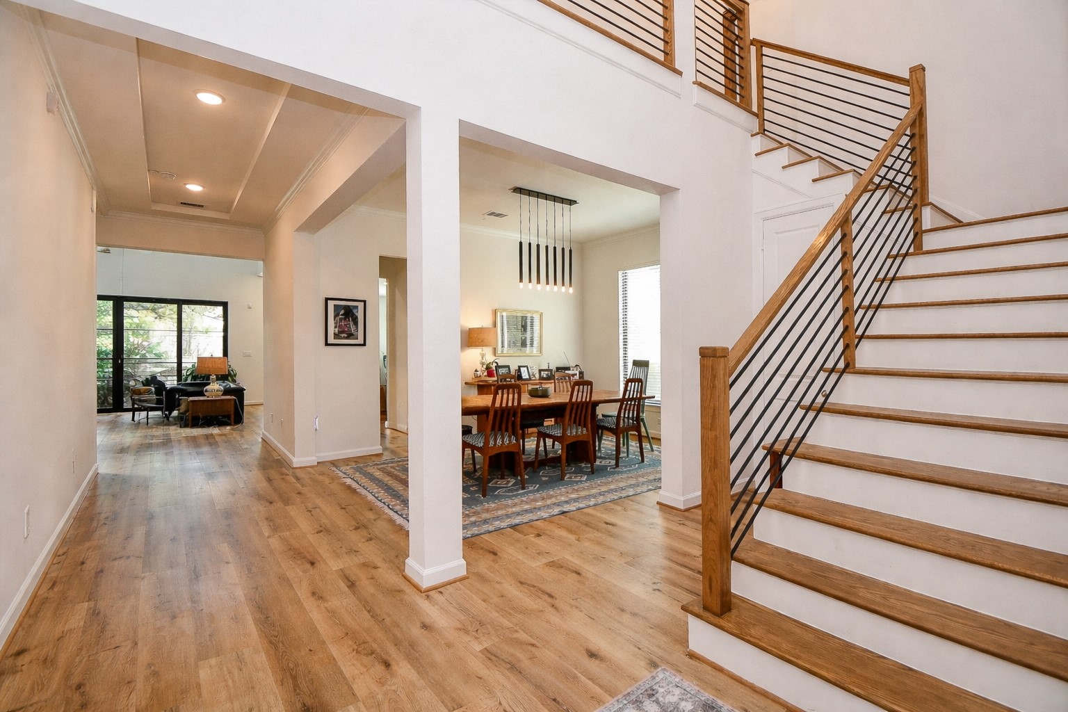 5315 Jason Street Houston, TX 77096 - Photo 2 of 39 Walk in and discovery a spacious, open-concept home with a warm wood floor, a modern staircase with metal railings, and a view into the open dining room and living area. Natural light streams through large windows, enhancing the inviting atmosphere.