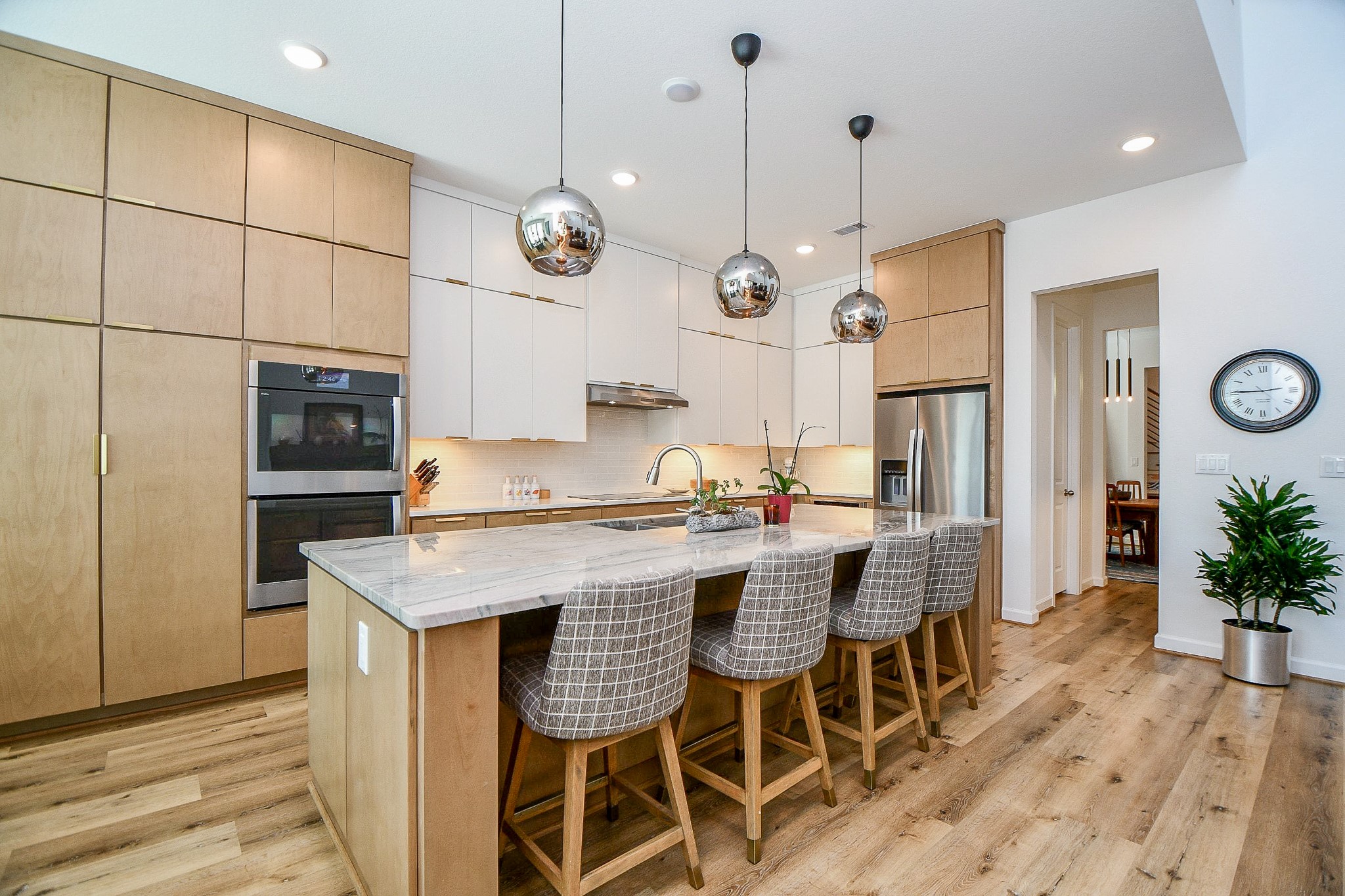 5315 Jason Street Houston, TX 77096 - Photo 5 of 39 The modern kitchen showcases sleek wood cabinetry, stainless steel appliances, and a spacious marble island with seating for four, complemented by pendant lighting and light wood flooring. An open, inviting layout is enhanced by an induction cooktop, double ovens with side-opening doors, and a whole-house vacuum system—blending style with everyday functionality.