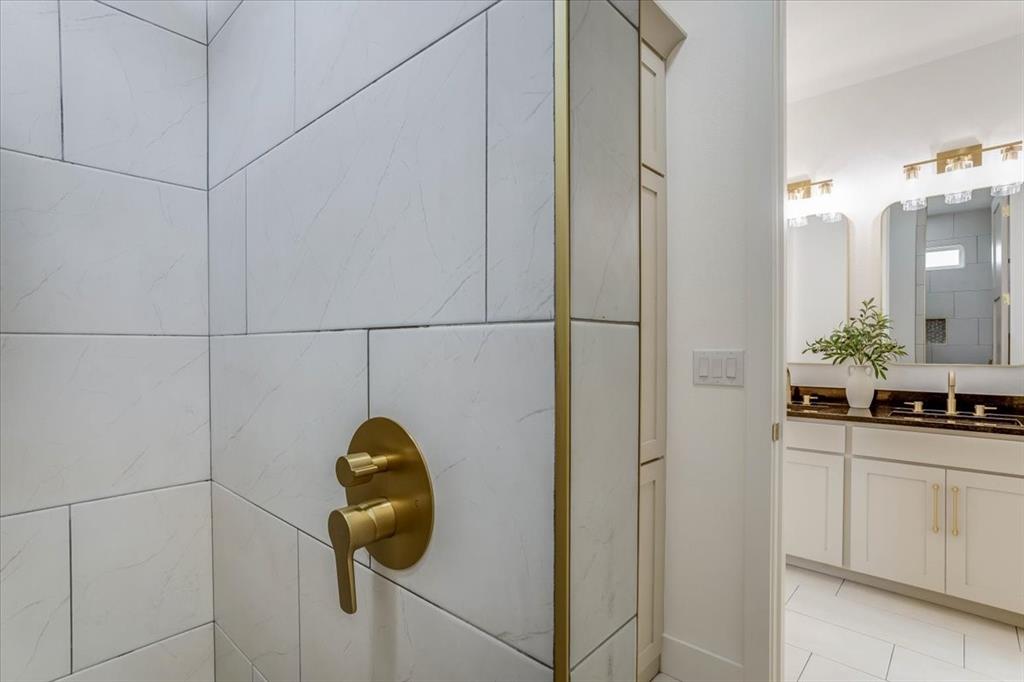242 Private Road Mount Pleasant, TX 75455 - Photo 31 of 40 White tiled shower with brass fixtures, built-in storage cabinet, dual vanity with dark countertops, and gold-tone sconce lighting