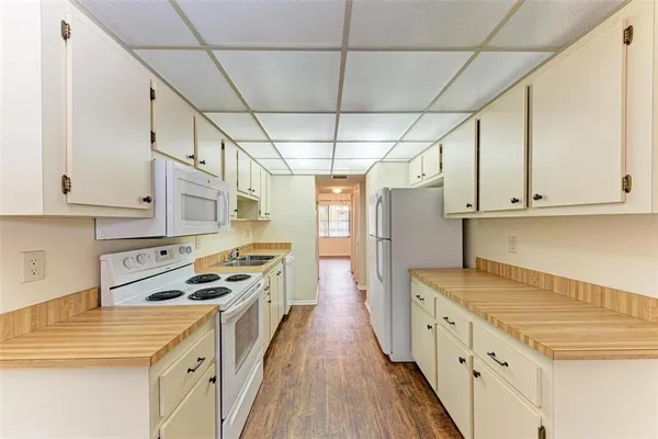 a kitchen with granite countertop a stove a sink a refrigerator and white cabinets with wooden floor