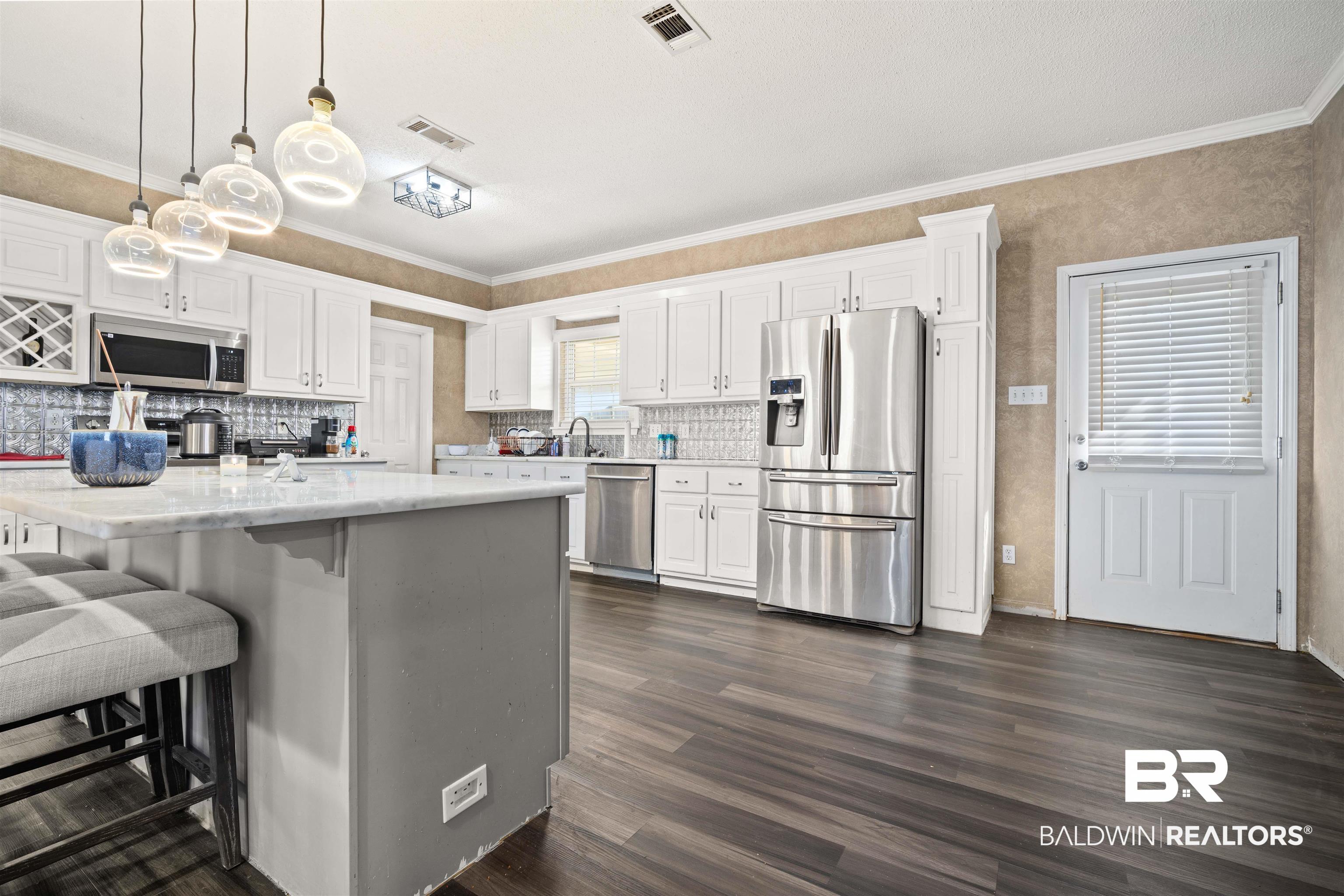 1609 Repoll Road Mobile, AL 36695 - Photo 7 of 22 Kitchen featuring white cabinets, stainless steel appliances, a kitchen bar, hanging light fixtures, and ornamental molding