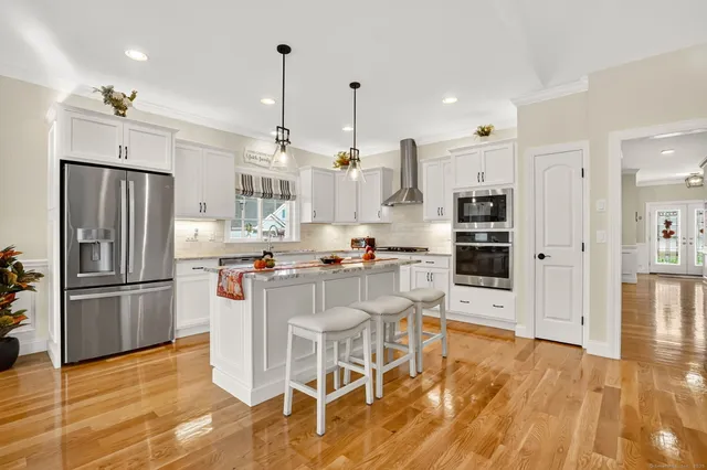 a kitchen with stainless steel appliances kitchen island granite countertop a refrigerator a stove and white cabinets with wooden floor