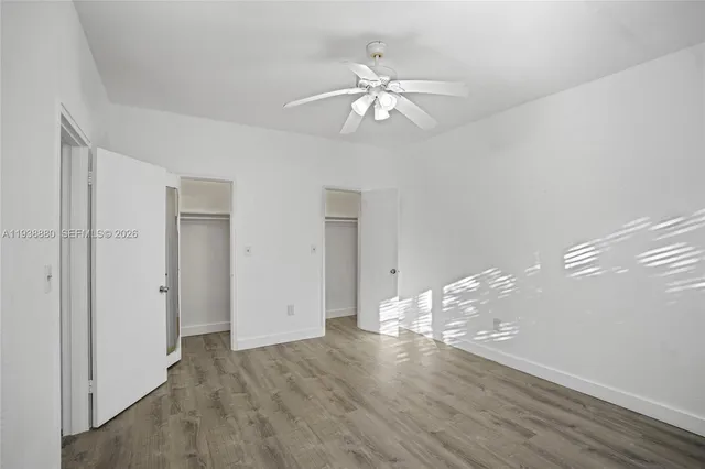 a view of an empty room with wooden floor and a ceiling fan