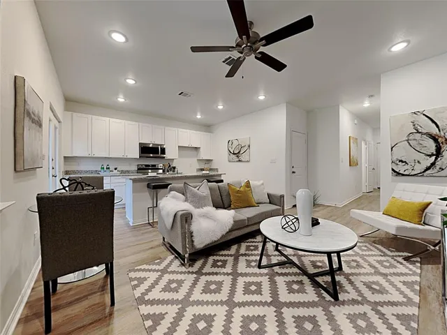 a living room with stainless steel appliances furniture a rug and a kitchen view