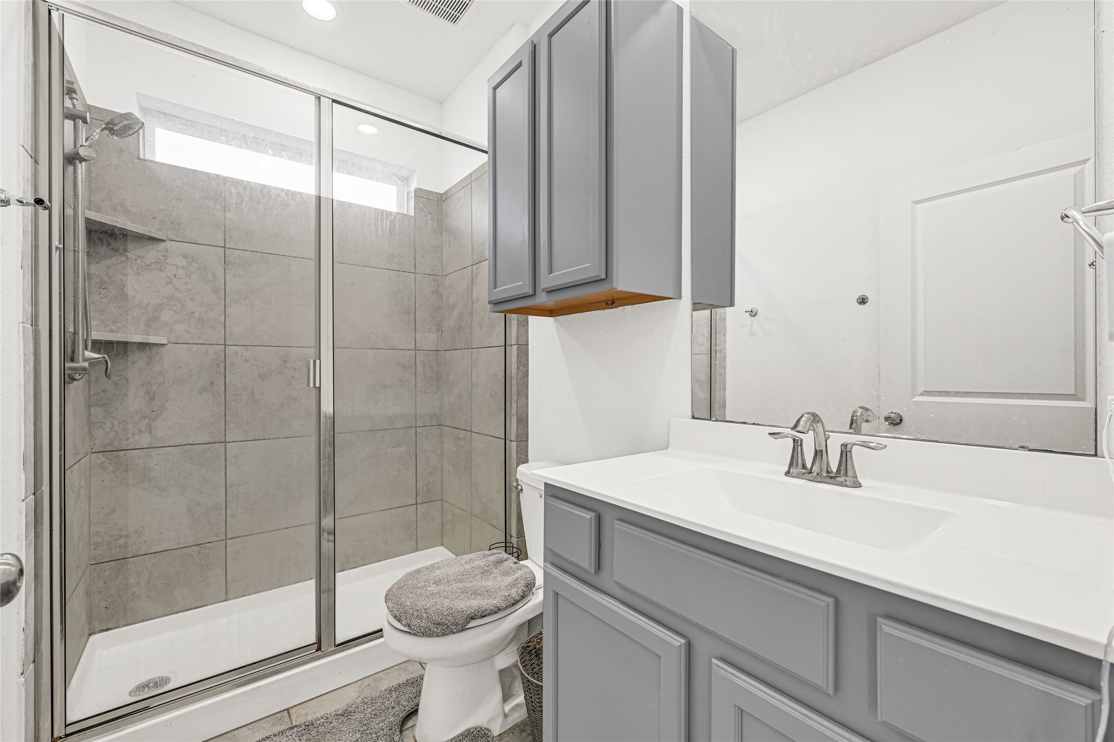 4307 Annandale Lane Rosharon, TX 77583 - Photo 23 of 31 This first floor bathroom is in the private apartment and features a modern design with a spacious glass-enclosed walk-in shower, gray tiled walls, and sleek fixtures. It includes a stylish vanity with ample storage and a large mirror, creating a clean and functional space.