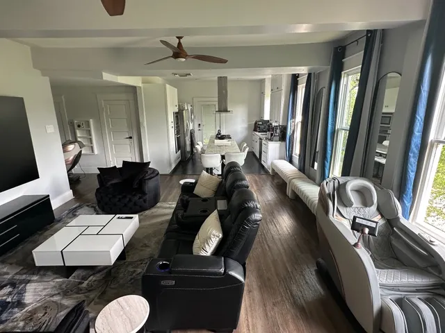 a living room with furniture two large window and wooden floor