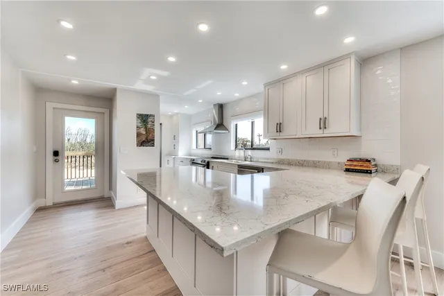 a kitchen with stainless steel appliances granite countertop a kitchen island a stove a sink a refrigerator and white cabinets with wooden floor