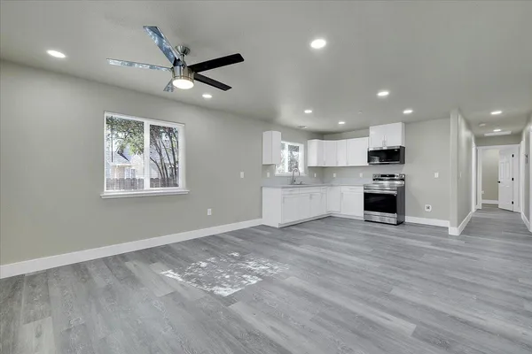 an empty room with wooden floor a ceiling fan and kitchen view