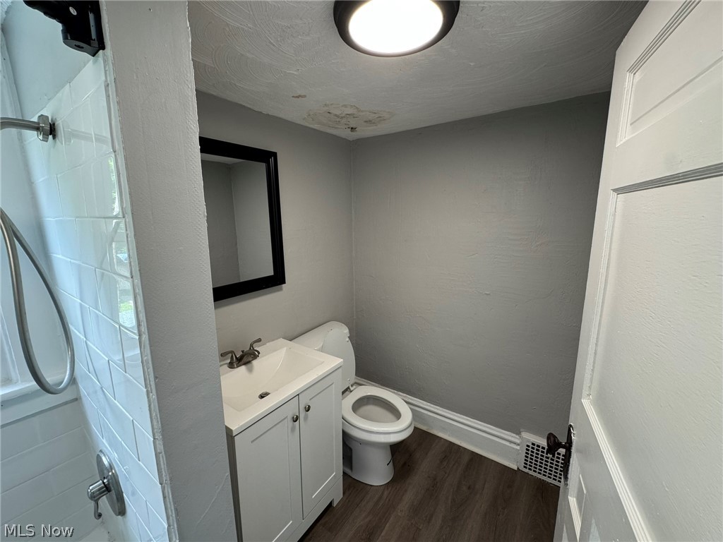 674-676 Carlysle Street Akron, OH 44310 - Photo 18 of 20 Bathroom featuring white subway tile shower, white vanity with integrated sink, wood-finish flooring, a toilet, and a framed mirror