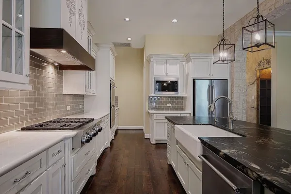 a kitchen with stainless steel appliances granite countertop a stove a sink dishwasher a refrigerator white cabinets and wooden floor