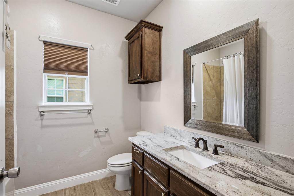 1502 Reed Street Greenville, TX 75401 - Photo 22 of 26 Bathroom featuring a wood-finish vanity with an integrated sink, granite-style countertop, and dark-bronze-finish fixtures