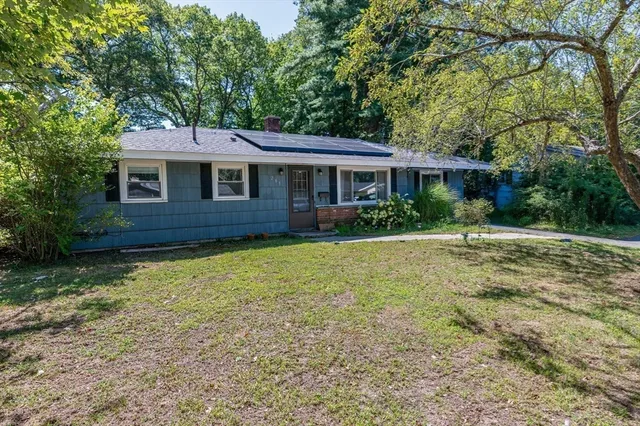 a brick house next to a yard with potted plants and large trees