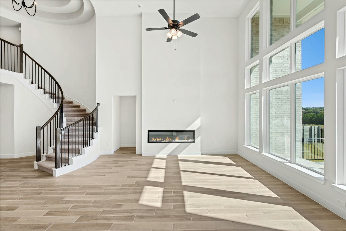 1533 Rodeo Ridge Drive Georgetown, TX 78628 - Photo 4 of 34 Unfurnished living room with wood finish floors, a high ceiling, stairway, a glass covered fireplace, and ceiling fan