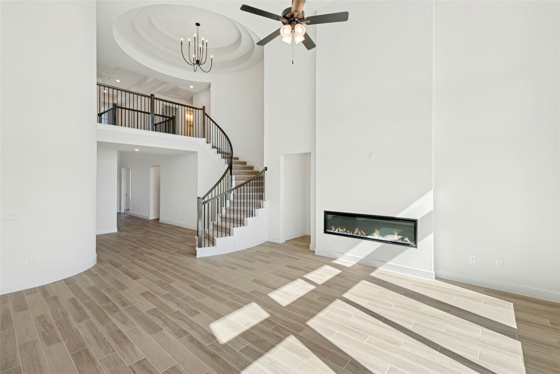1533 Rodeo Ridge Drive Georgetown, TX 78628 - Photo 5 of 34 Unfurnished living room with a high ceiling, a glass covered fireplace, stairway, wood tiled floors, and ceiling fan