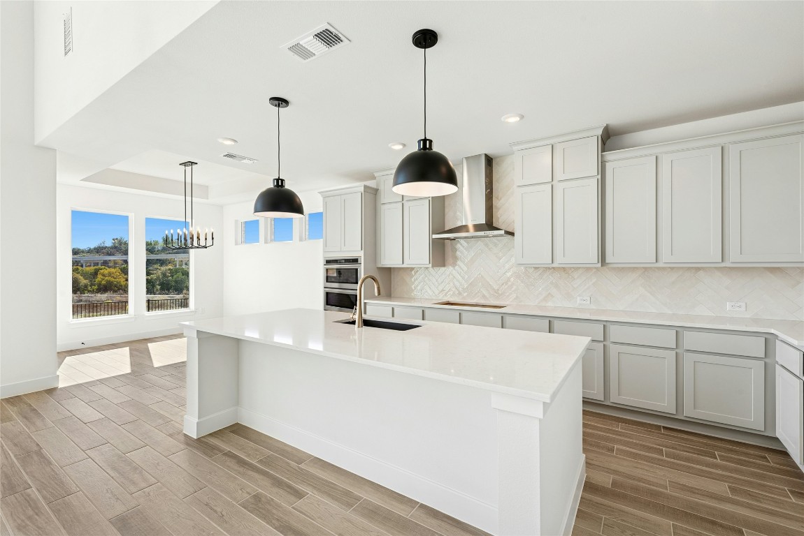 1533 Rodeo Ridge Drive Georgetown, TX 78628 - Photo 7 of 34 Kitchen featuring wood finish floors, wall chimney range hood, decorative light fixtures, light stone countertops, and recessed lighting
