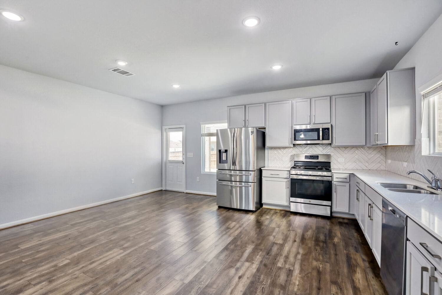 6601 Avila Way Pflugerville, TX 78660 - Photo 7 of 28 Kitchen featuring stainless steel appliances, gray cabinets, light stone countertops, backsplash, and dark wood finished floors