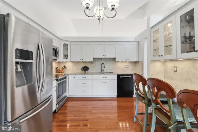 a kitchen with stainless steel appliances granite countertop a refrigerator a stove a sink a dining table and chairs with wooden floor