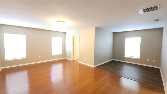 an empty room with wooden floor and windows with curtains