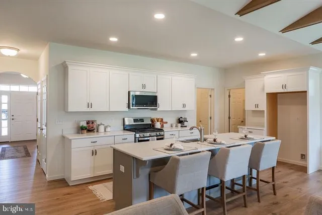 a kitchen with stainless steel appliances kitchen island granite countertop a sink a stove a refrigerator and white cabinets with wooden floor