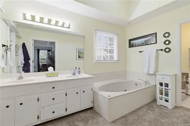 a bathroom with a bathtub a double vanity sink a window and a mirror