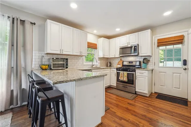 a kitchen with stainless steel appliances granite countertop a stove top oven a sink dishwasher and a refrigerator with wooden floor