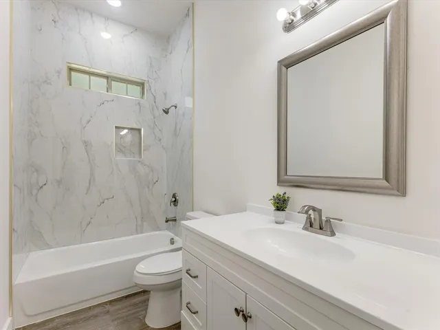 a bathroom with a bathtub shower sink vanity mirror and toilet