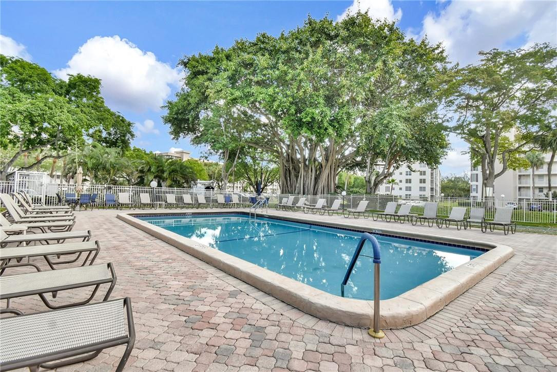 2601 South Course Drive, Unit 409 Pompano Beach, FL 33069 - Photo 35 of 58 a view of swimming pool that has lawn chairs with plants and trees