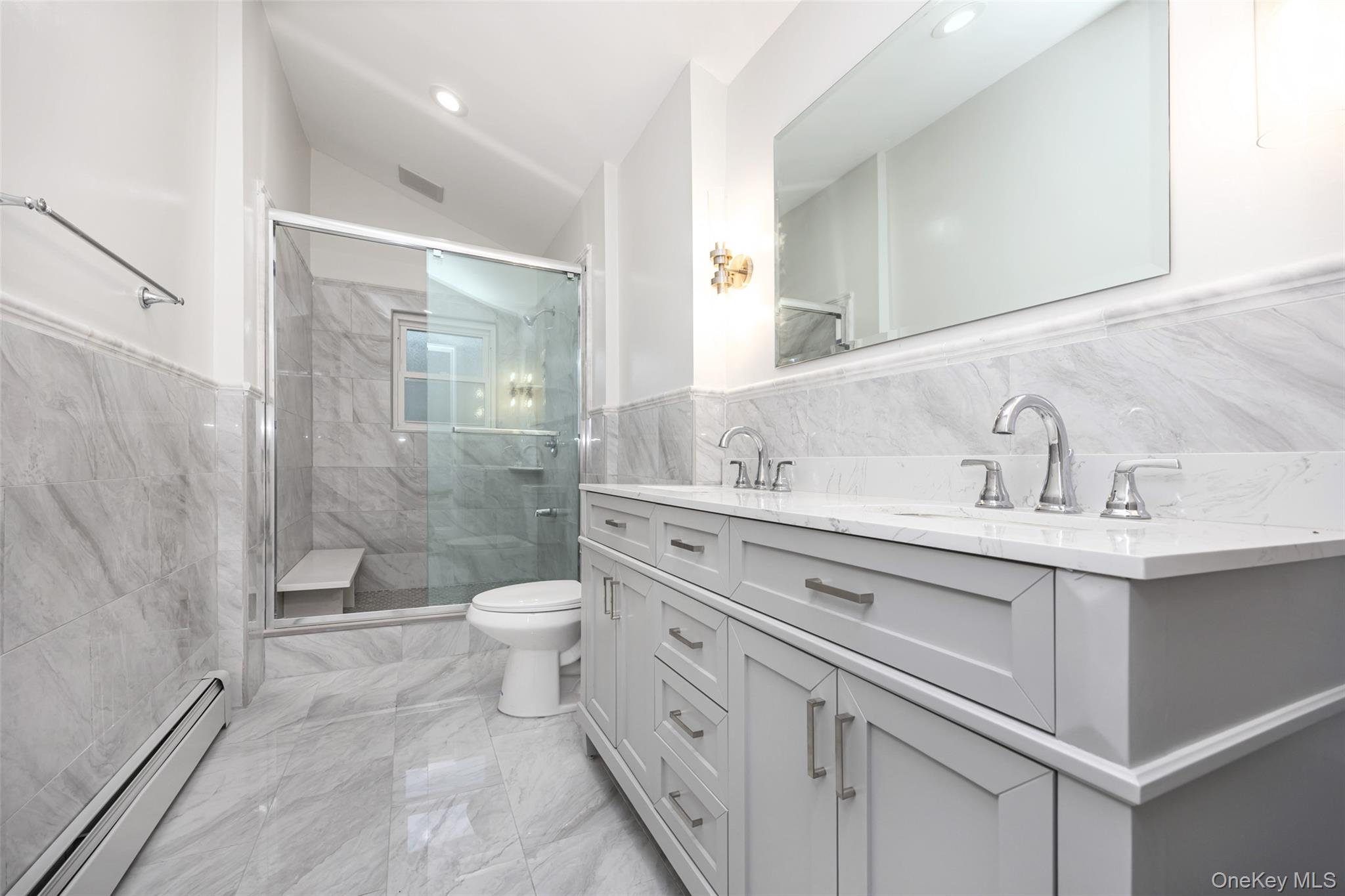 36 Red Spring Lane Glen Cove, NY 11542 - Photo 16 of 33 Primary bathroom – Luxurious retreat featuring a deep soaking tub, glass-enclosed shower, and elegant tilework. Decorative vanity and wall sconces add a classic, timeless touch.