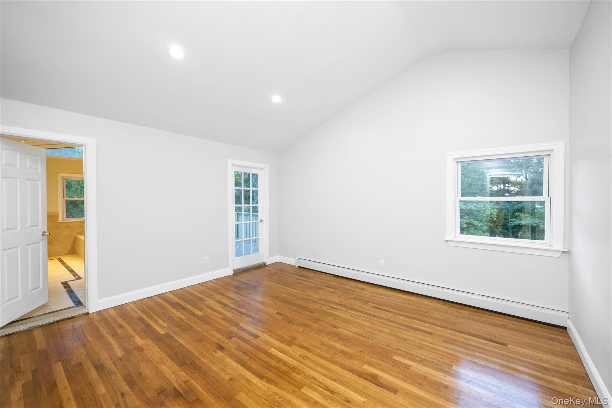 36 Red Spring Lane Glen Cove, NY 11542 - Photo 18 of 33 Primary bedroom – Spacious, sun-filled suite with hardwood floors, recessed lighting, and neutral tones. Private door provides direct access to the upper deck.