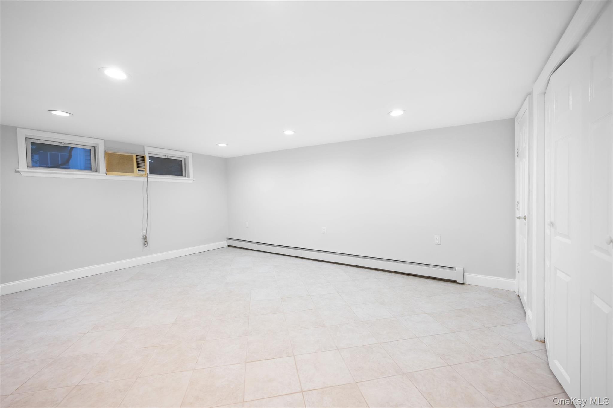 36 Red Spring Lane Glen Cove, NY 11542 - Photo 23 of 33 Lower-Level Family Room – Spacious and freshly painted, this versatile room offers recessed lighting, neutral tile flooring, and sliding doors opening to the backyard patio—ideal for gatherings or recreation.