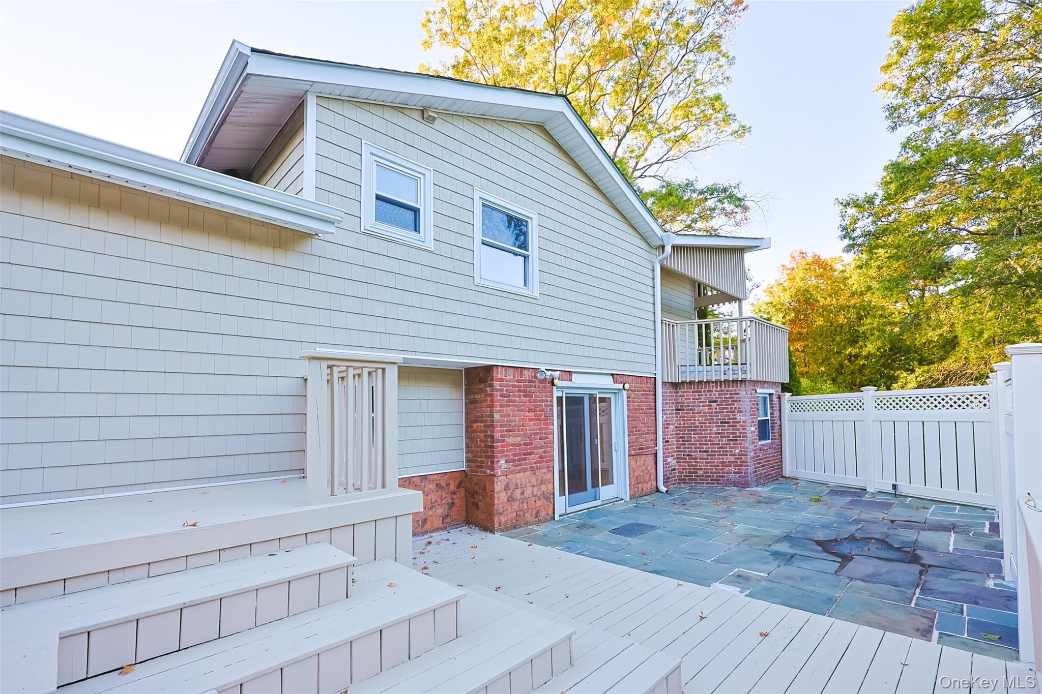 36 Red Spring Lane Glen Cove, NY 11542 - Photo 29 of 33 Rear Exterior – The back of the home features brick and shingle siding with direct walk-out access from the lower level, connecting to a private patio.