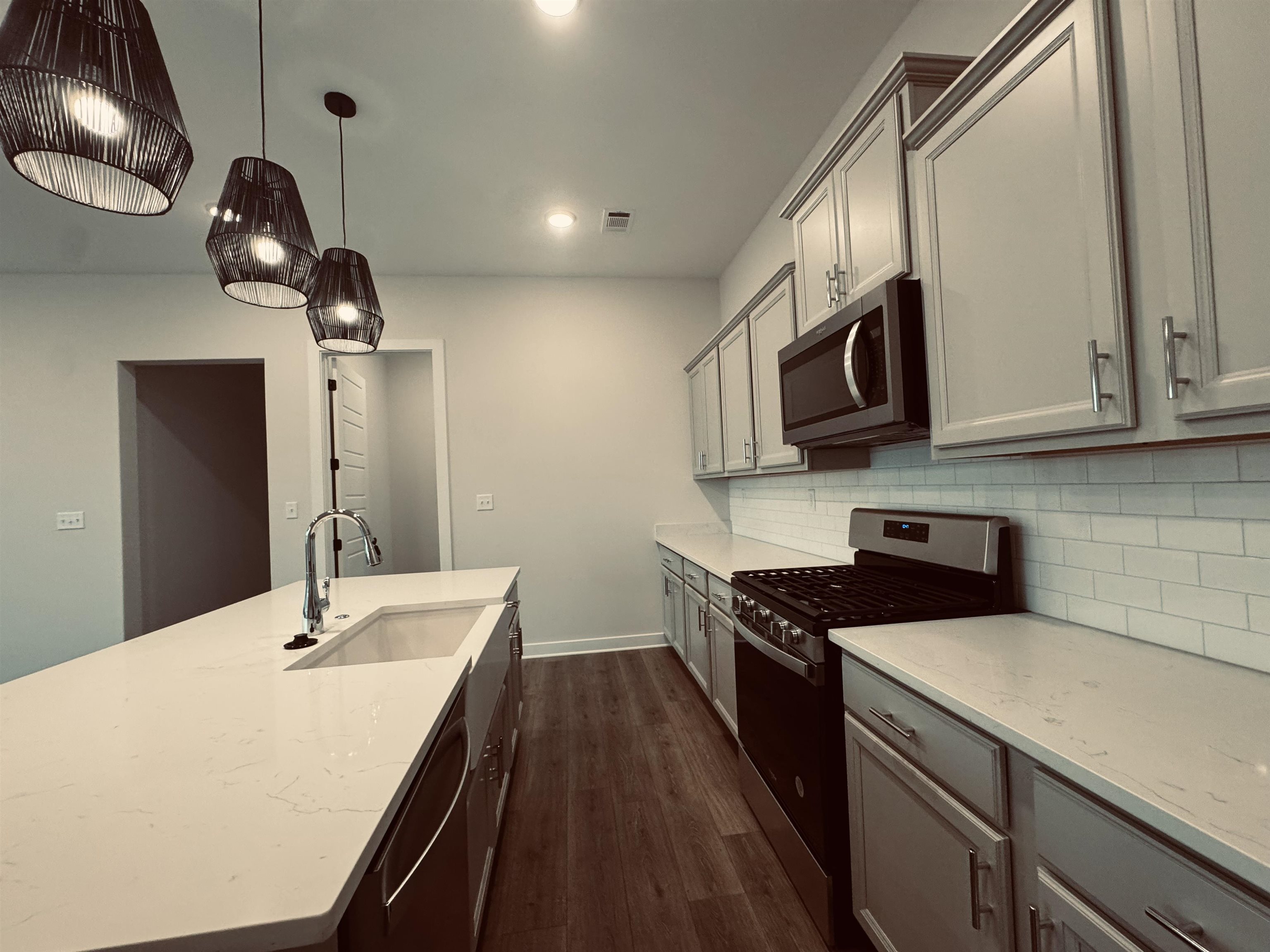 Kitchen featuring appliances with stainless steel finishes, light stone counters, sink, pendant lighting, and dark hardwood / wood-style floors