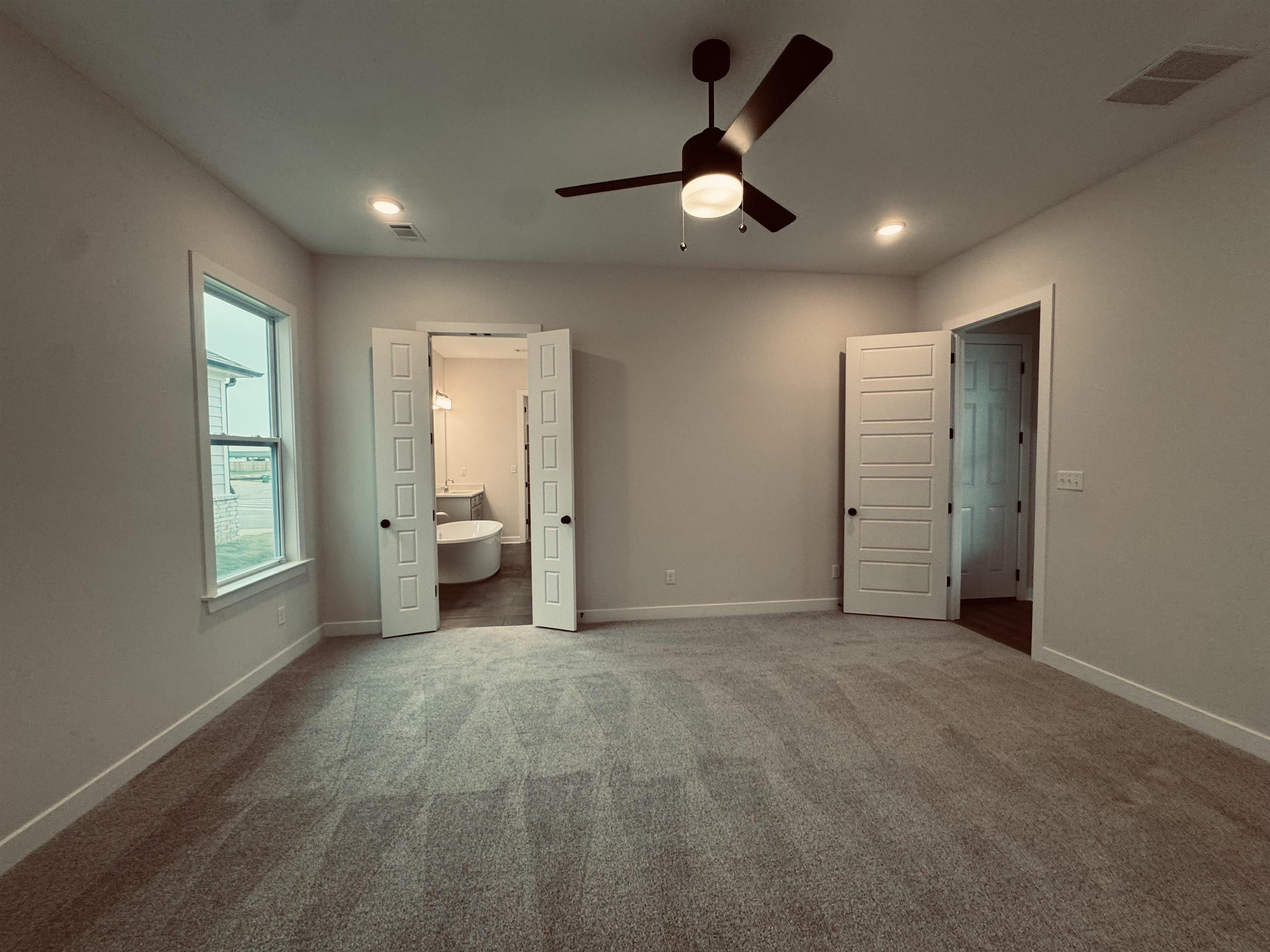 Unfurnished bedroom with ceiling fan, carpet floors, and ensuite bathroom