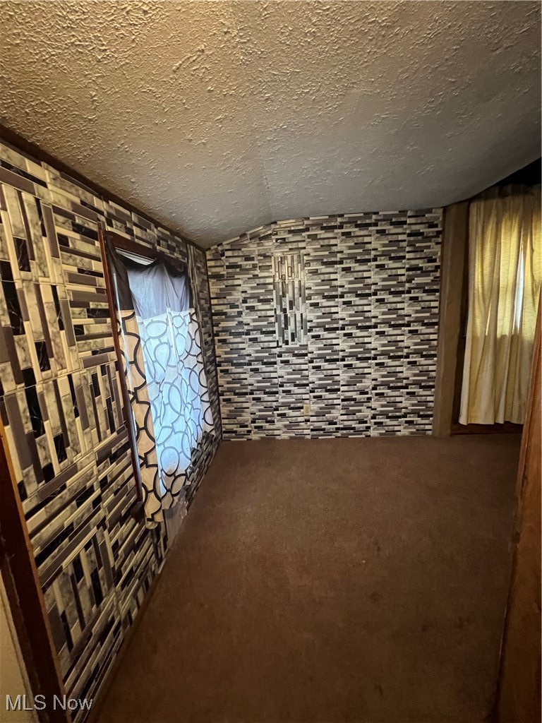 1334 Penhurst Road Cleveland, OH 44110 - Photo 9 of 20 Empty room featuring a textured ceiling, vaulted ceiling, and carpet