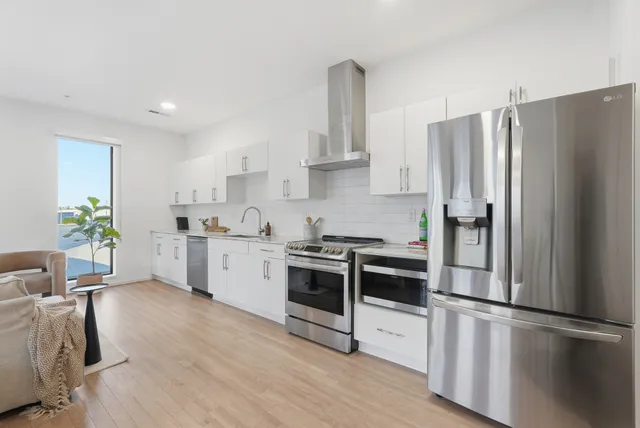 a kitchen with stainless steel appliances a refrigerator a stove a sink and white cabinets with wooden floor