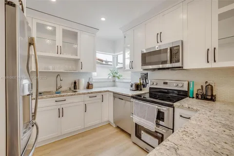 a kitchen with stainless steel appliances granite countertop white cabinets a sink a stove a refrigerator and microwave with wooden floor