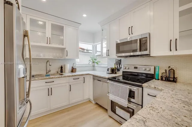 a kitchen with stainless steel appliances granite countertop white cabinets a sink a stove a refrigerator and microwave with wooden floor