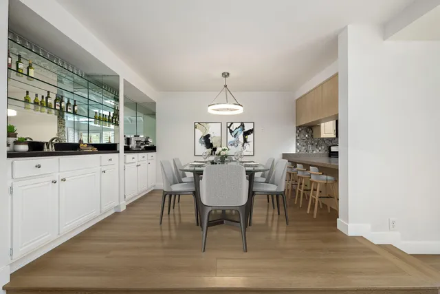 a dining room with wooden floor and white kitchen