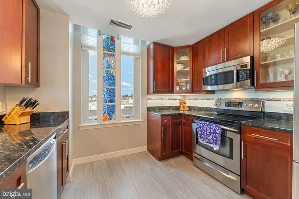 a kitchen with stainless steel appliances granite countertop a stove top oven a sink dishwasher a microwave oven and a refrigerator with wooden cabinets